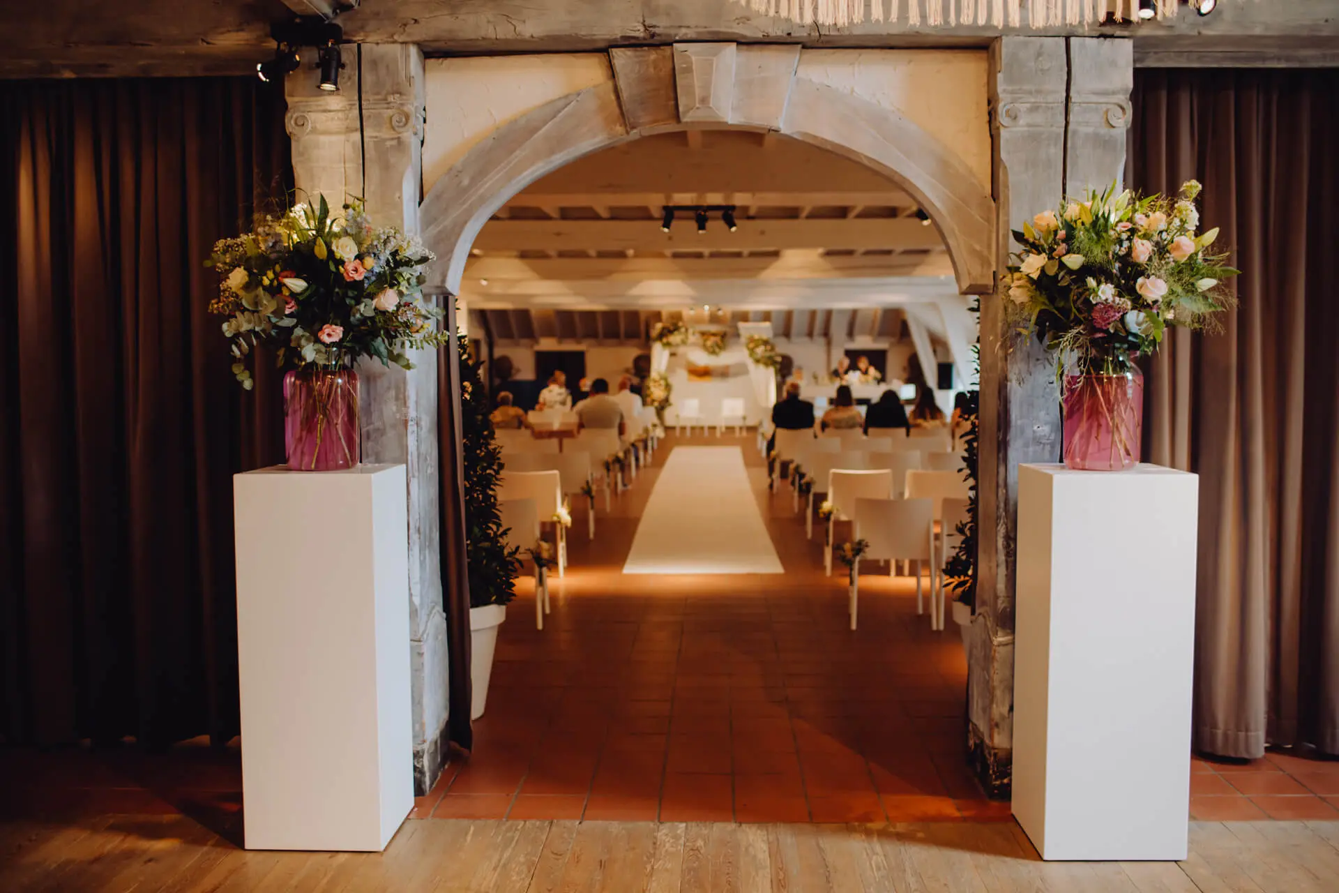Doorkijk door de boog naar de kleine zaal, opgesteld voor een ceremonie met boeketten op zuilen