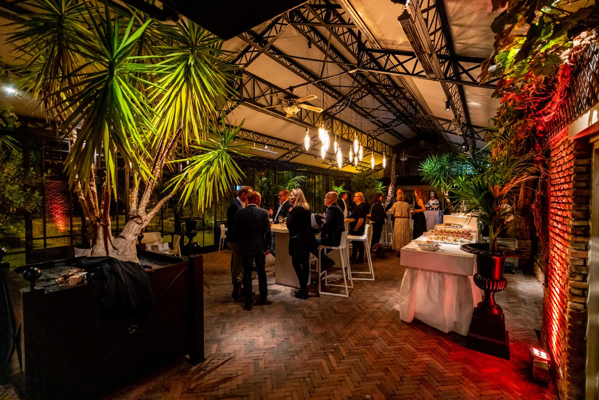 Gasten tijdens een avondreceptie in de sfeervol verlichte orangerie