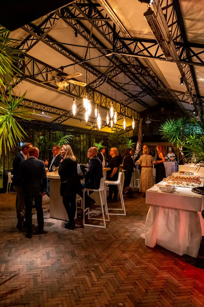 Avondreceptie in de orangerie, met gasten aan hoge tafels tussen de palmbomen