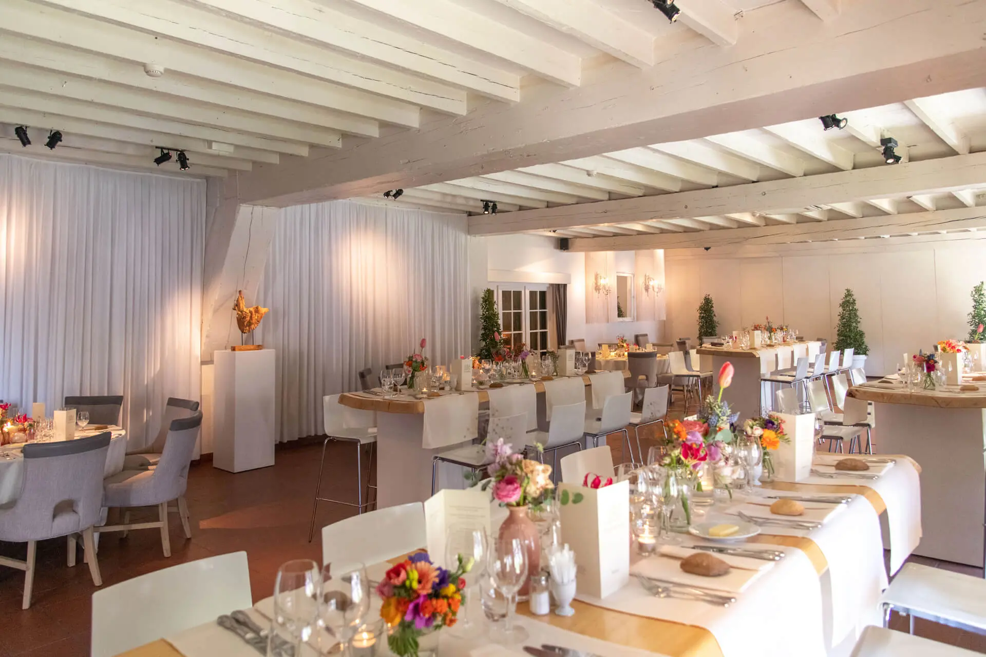 Kleine zaal gedekt voor een diner met lange tafels en kleurrijke bloemen