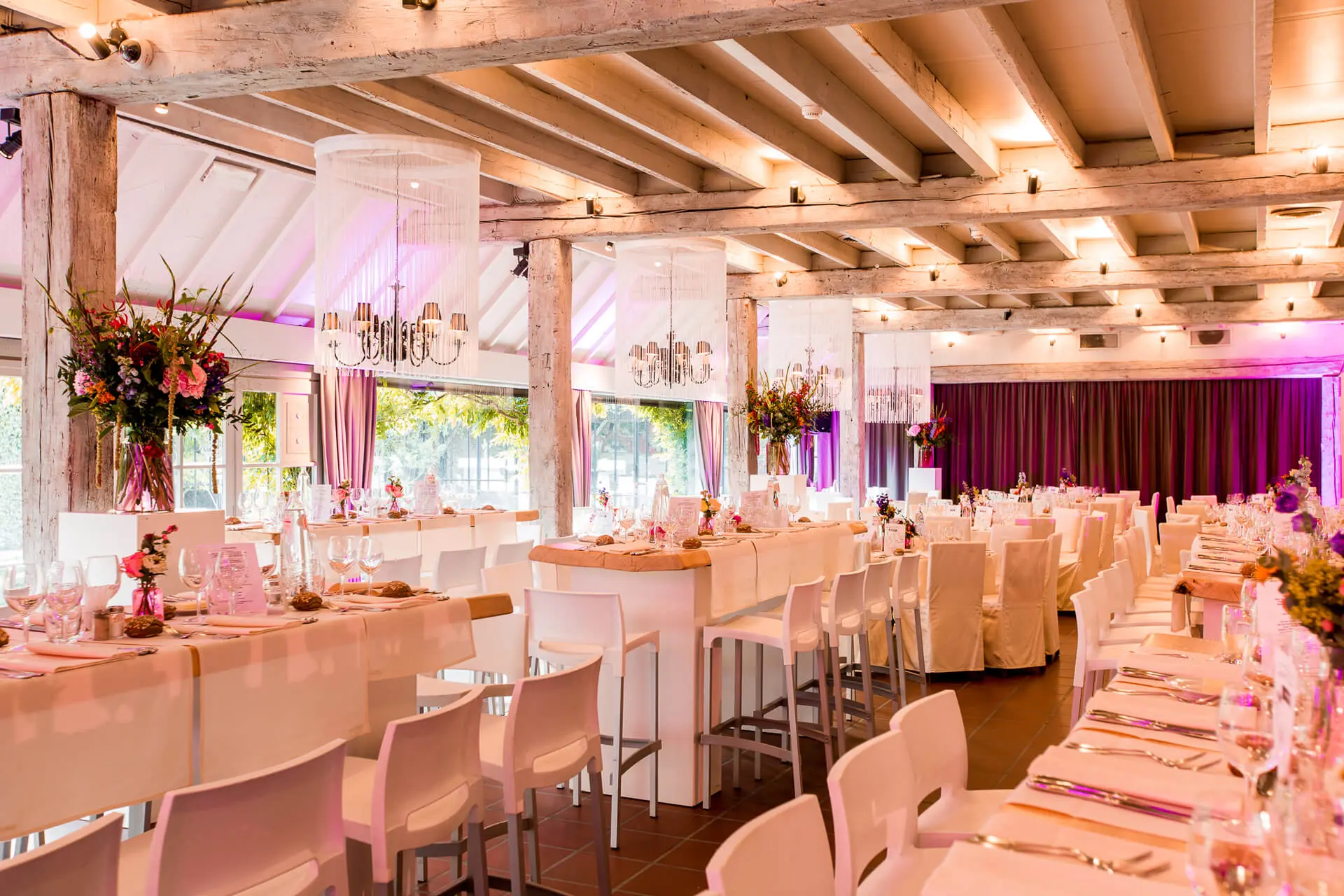Grote zaal met lange gedekte tafels, hoge tafels en bloemstukken