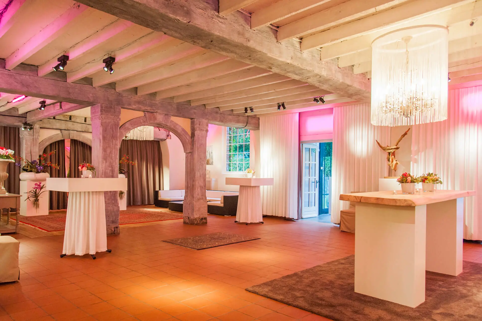 Aperitiefgedeelte van de kleine zaal met hoge tafels, houten balken en roze verlichting