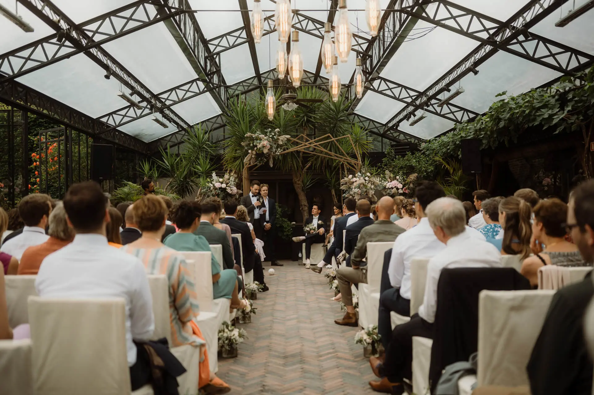 Gasten volgen een huwelijksceremonie in de orangerie van de grote zaal