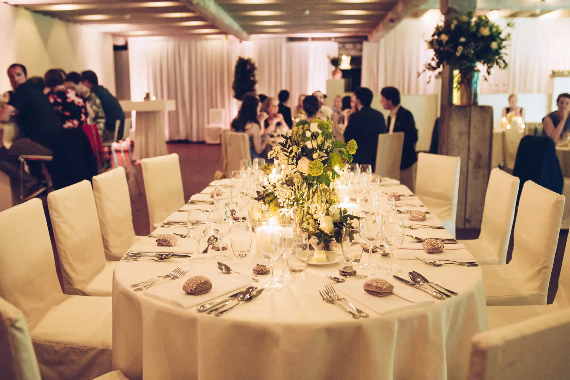 Gasten aan tafel tijdens een huwelijksdiner in de grote zaal, met een ovale eretafel op de voorgrond