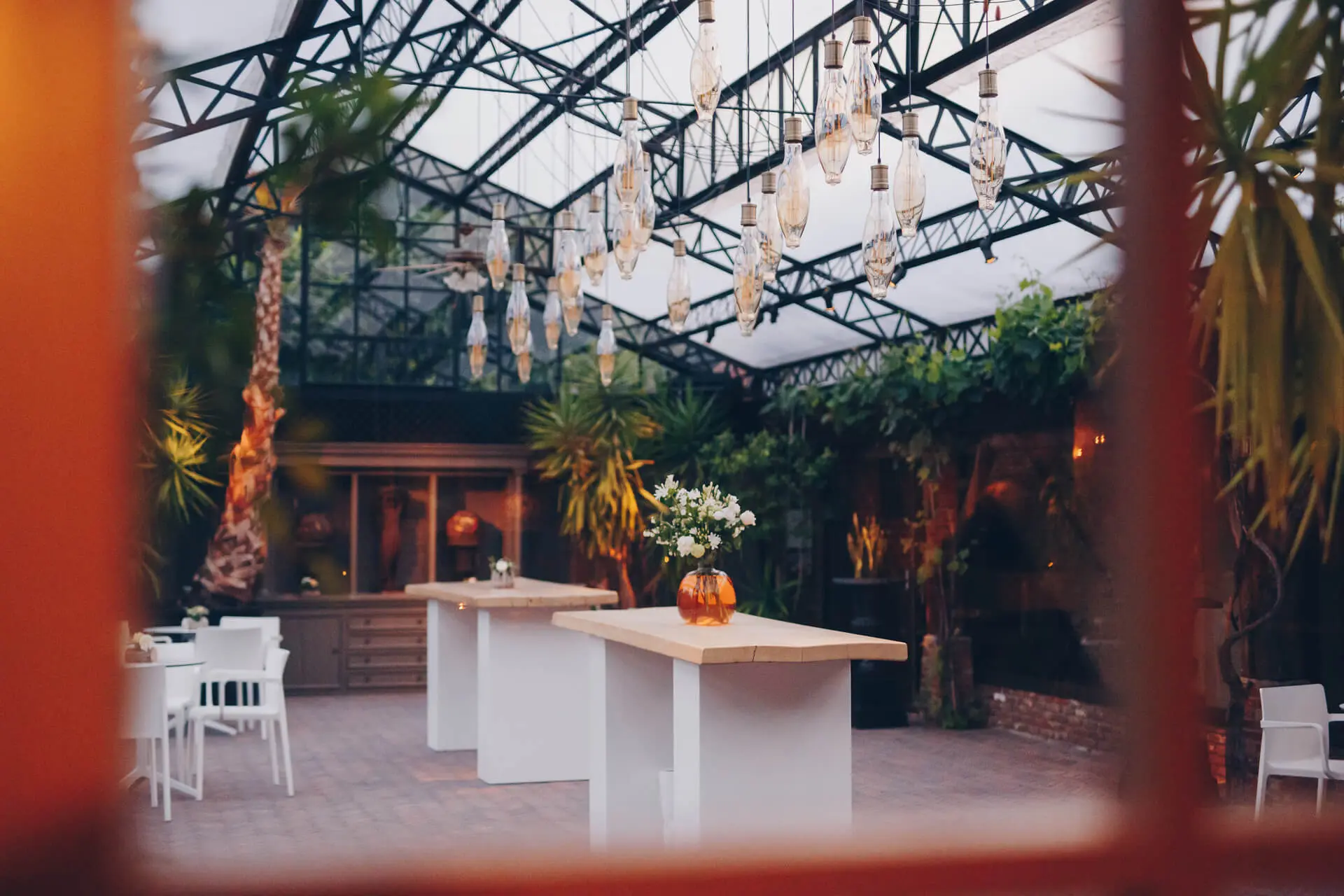 Doorkijk naar de orangerie van de grote zaal met hoge tafels, palmen en hanglampen