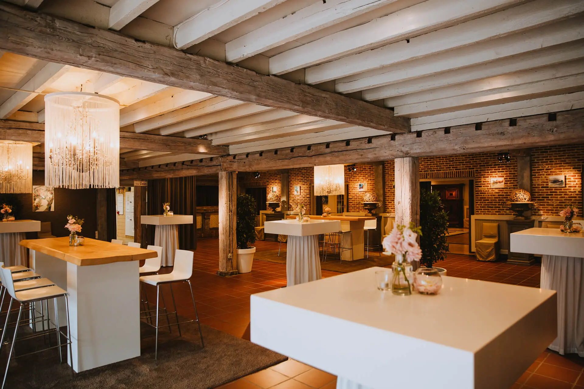 Aperitiefgedeelte van de grote zaal met hoge tafels, kroonluchters en houten balken