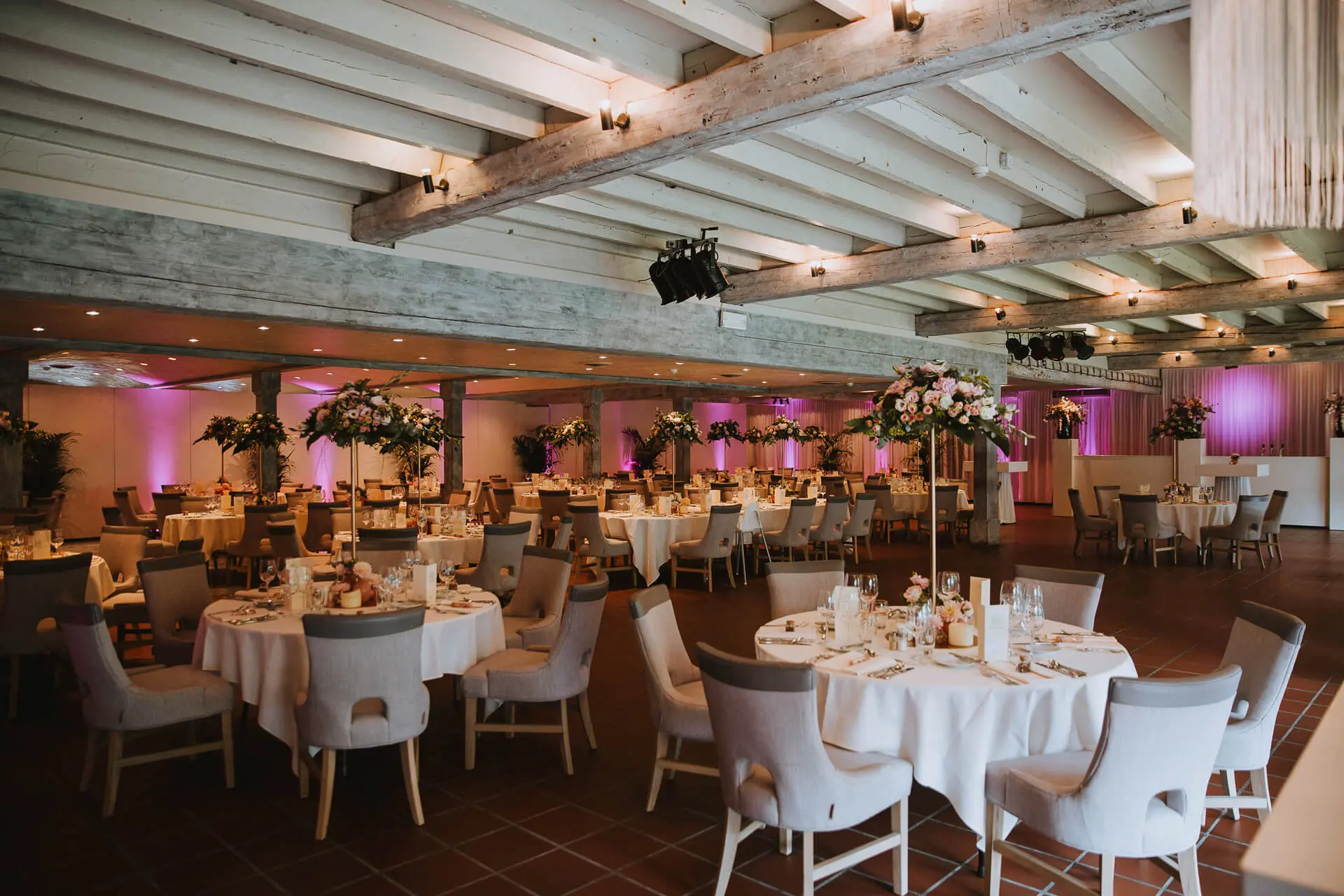 Grote zaal gedekt voor een huwelijksdiner met ronde tafels en hoge bloemstukken