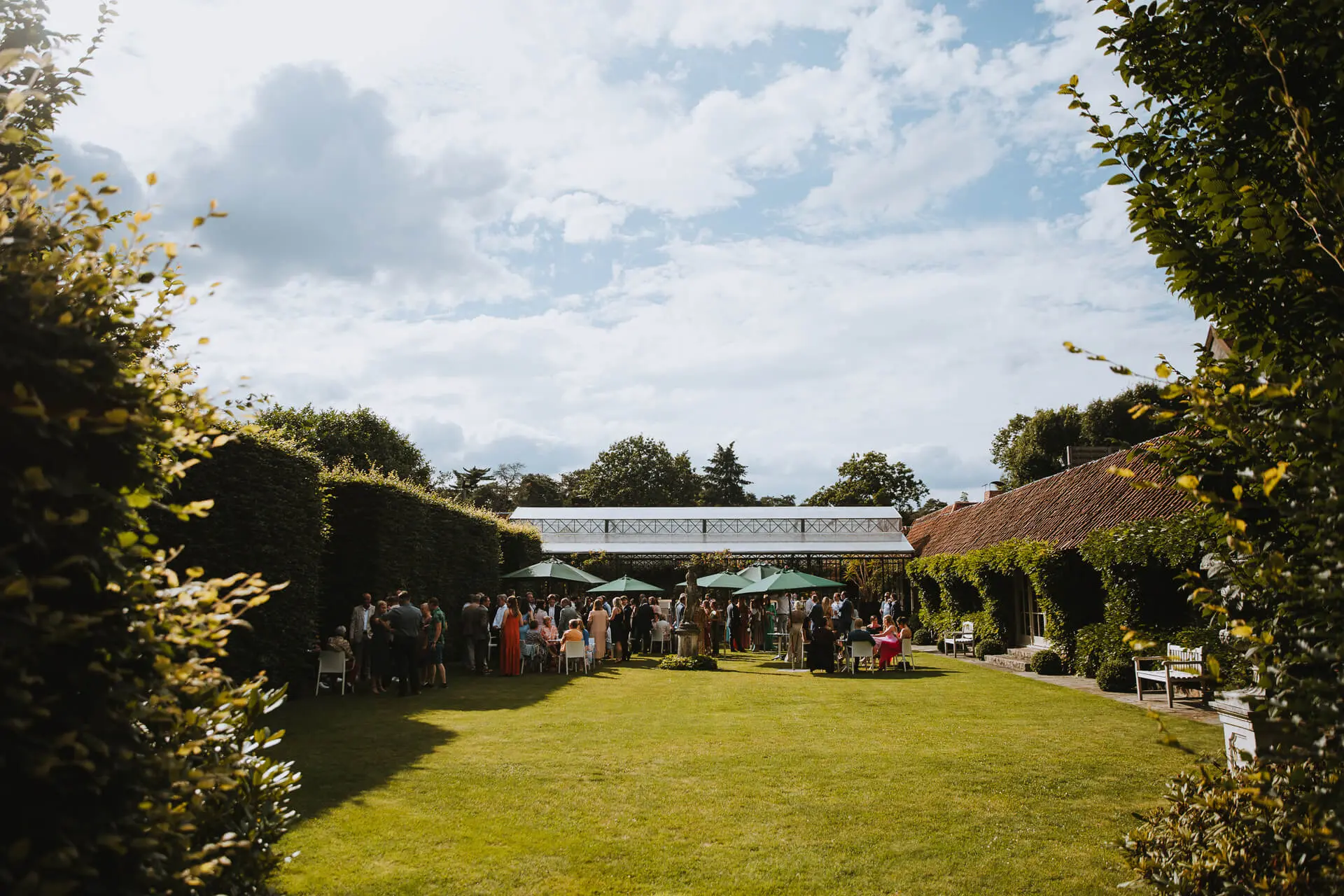 Gasten genieten van het aperitief in de groene tuin, omzoomd door hoge hagen