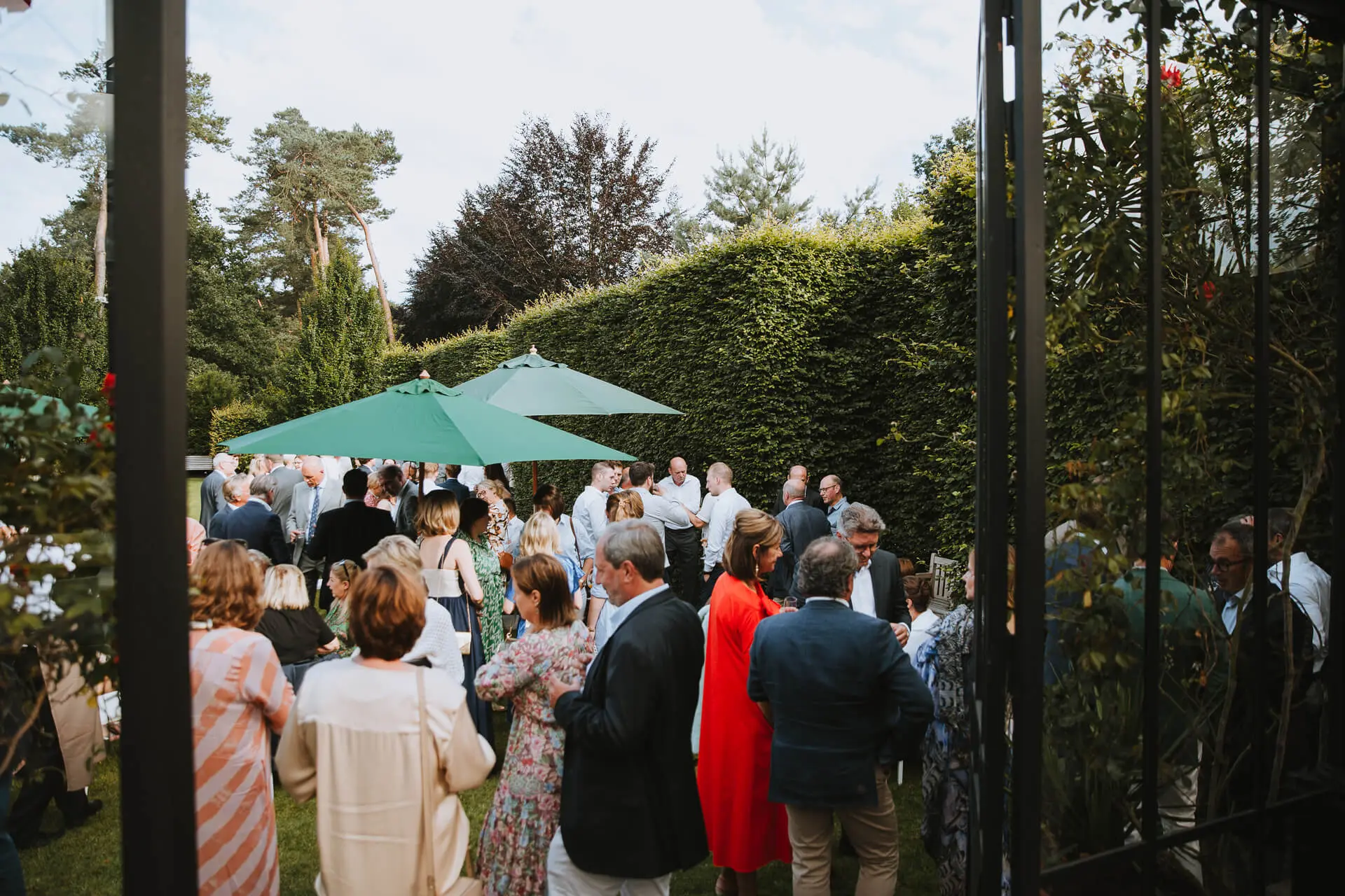Gasten genieten van het aperitief in de tuin onder groene parasols