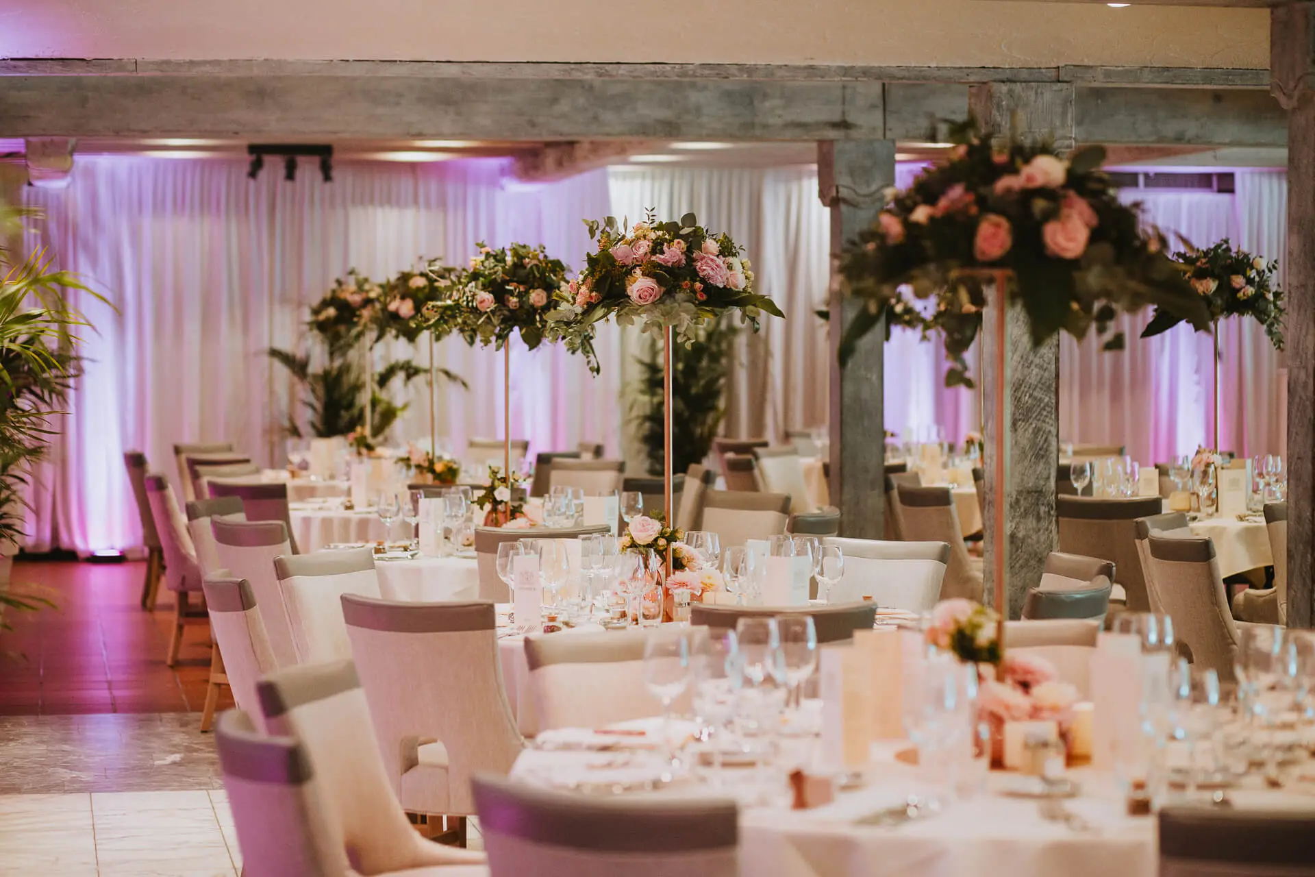 Gedekte tafels met hoge bloemstukken in roze tinten in de grote zaal