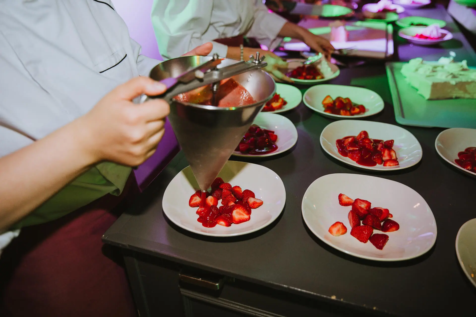 Kok schept verse aardbeien op bordjes voor het dessert
