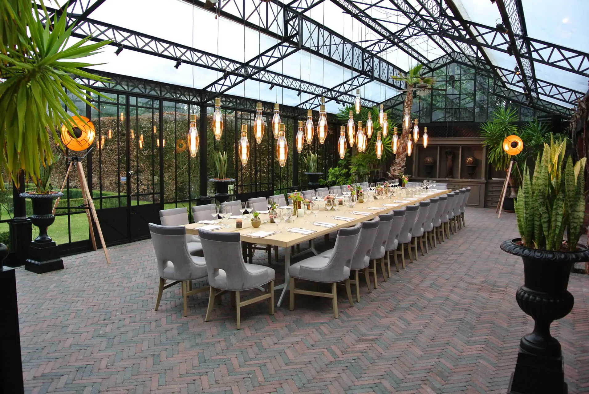 Lange houten tafel met grijze stoelen onder hanglampen in de orangerie