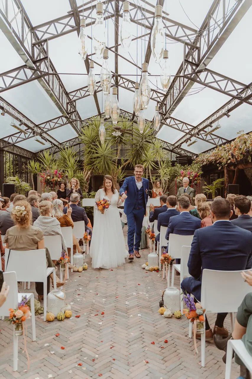 Bruidspaar wandelt door het middenpad van de orangerie tijdens een herfstceremonie