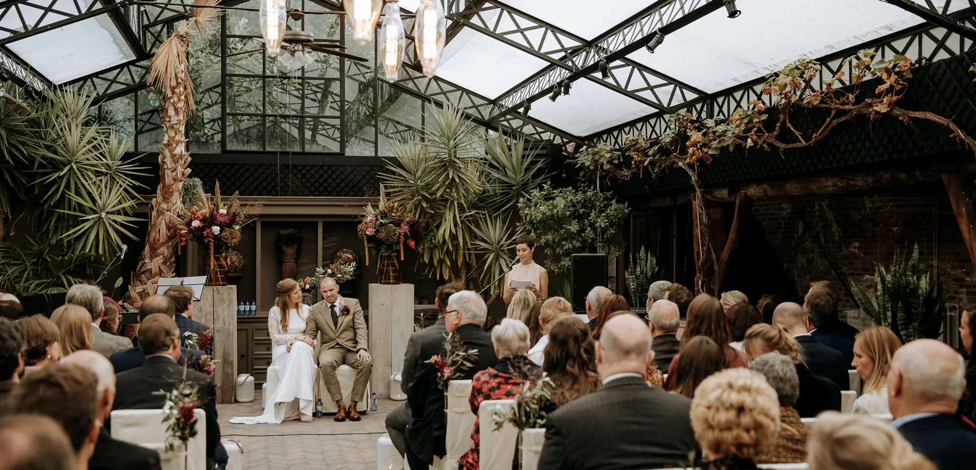 Huwelijksceremonie in de orangerie met herfstdecoratie en palmen onder het glazen dak