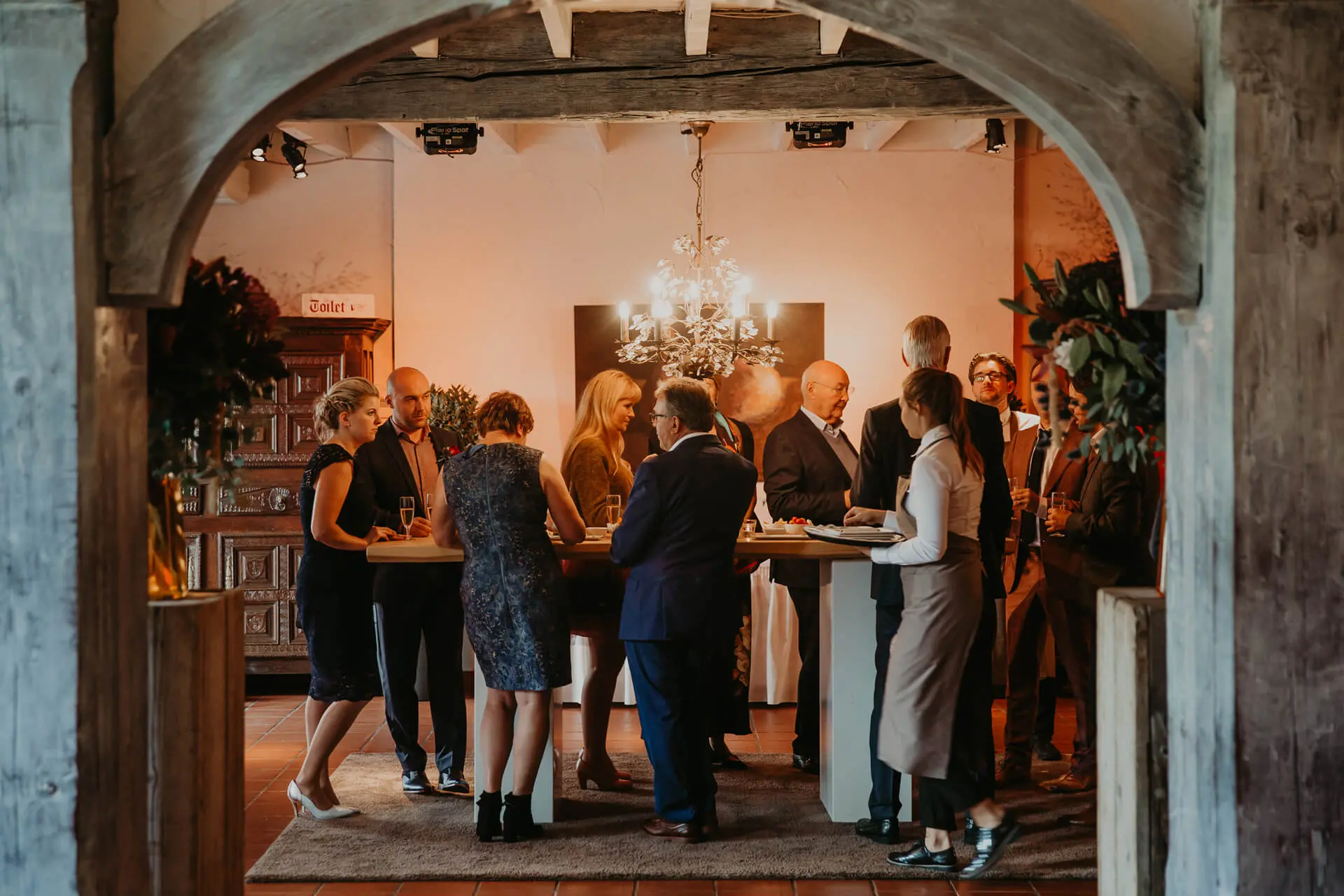 Gasten tijdens het aperitief in de kleine zaal, gezien door de poort