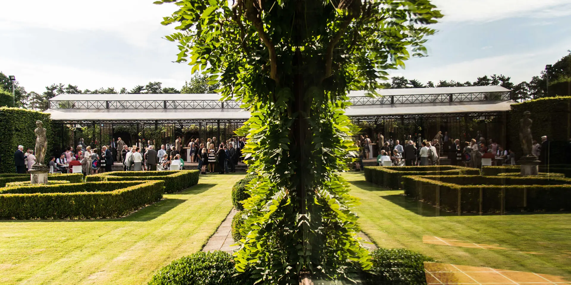 Tuin met buxushagen en gasten op het terras van de grote zaal