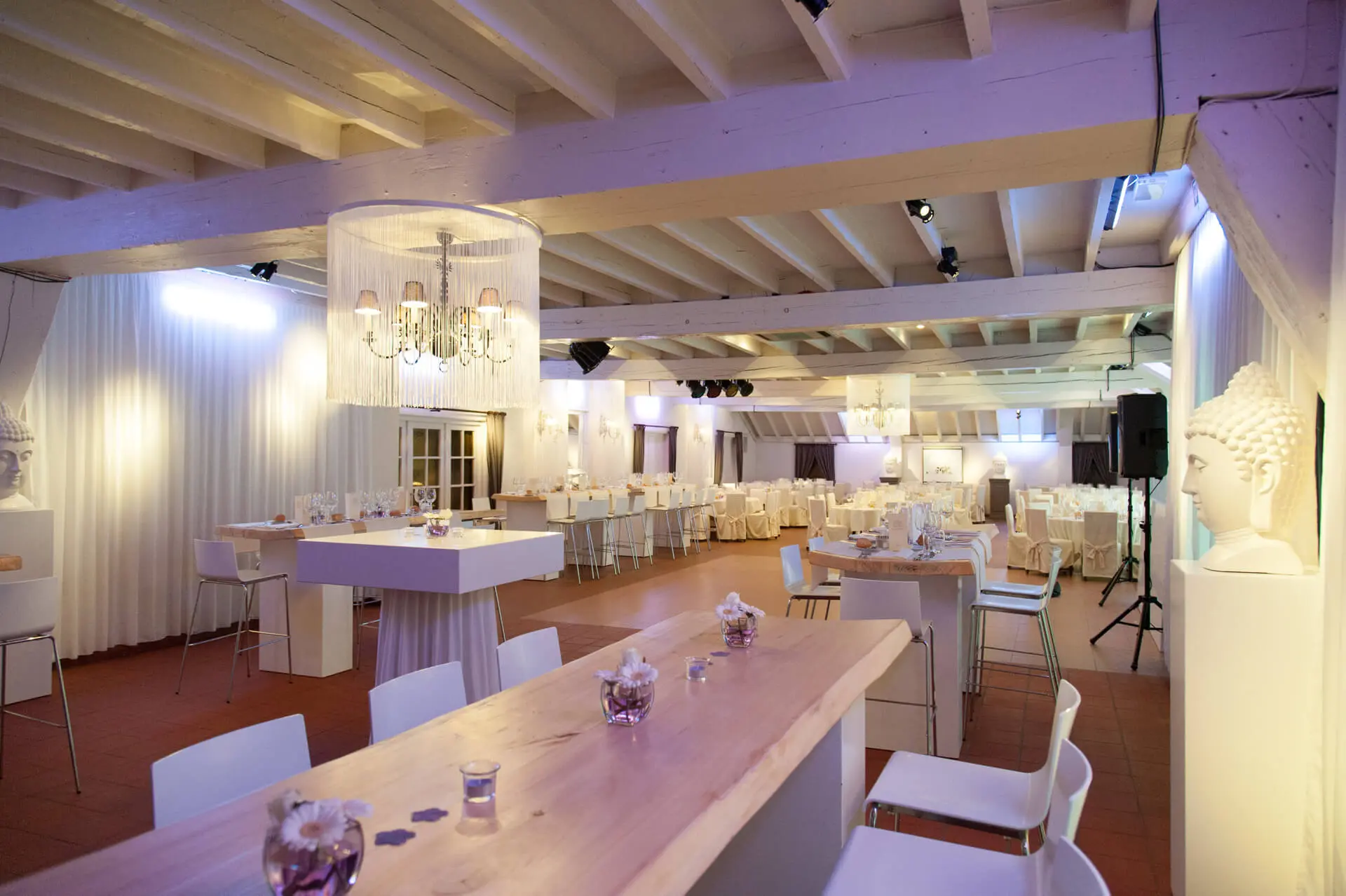 Kleine zaal met een mix van hoge en lage tafels, witte gordijnen en een kroonluchter
