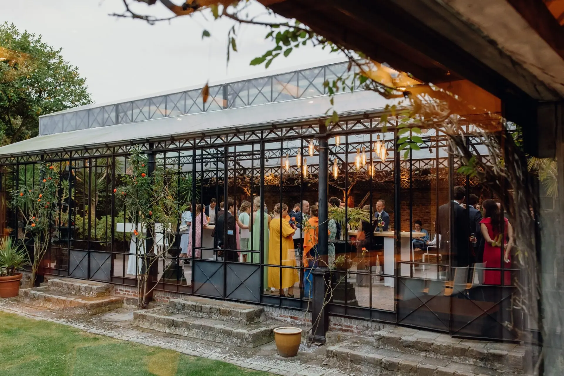 Gasten tijdens een receptie in de grote orangerie, gezien vanuit de tuin