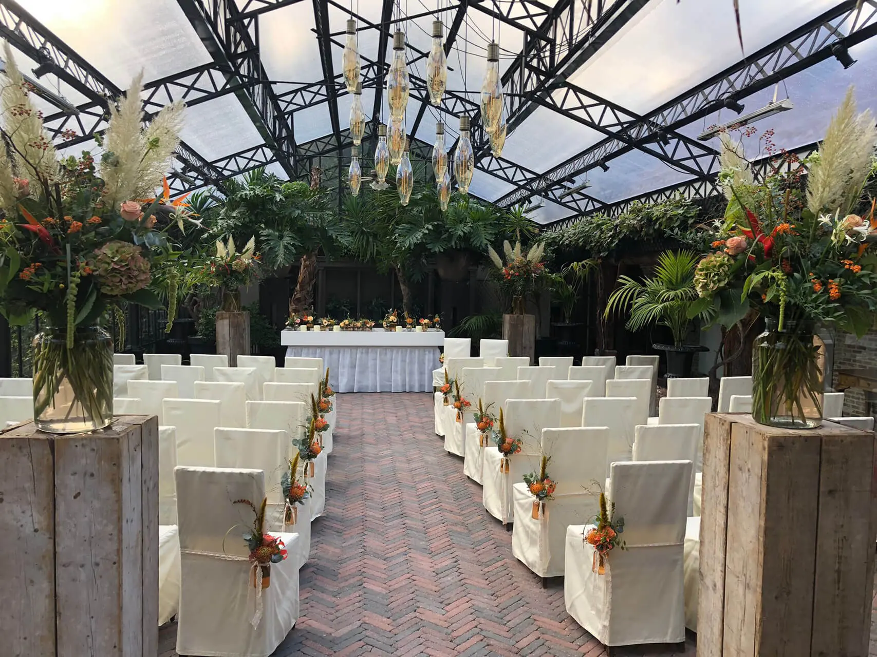 Orangerie van de grote zaal klaargezet voor een ceremonie met witte stoelen en boeketten met pampasgras