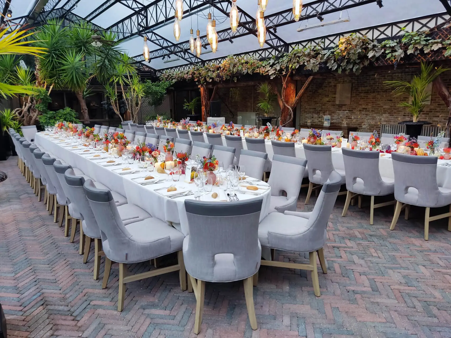 Lange gedekte tafels met grijze fauteuils en herfstbloemen in de orangerie van de grote zaal
