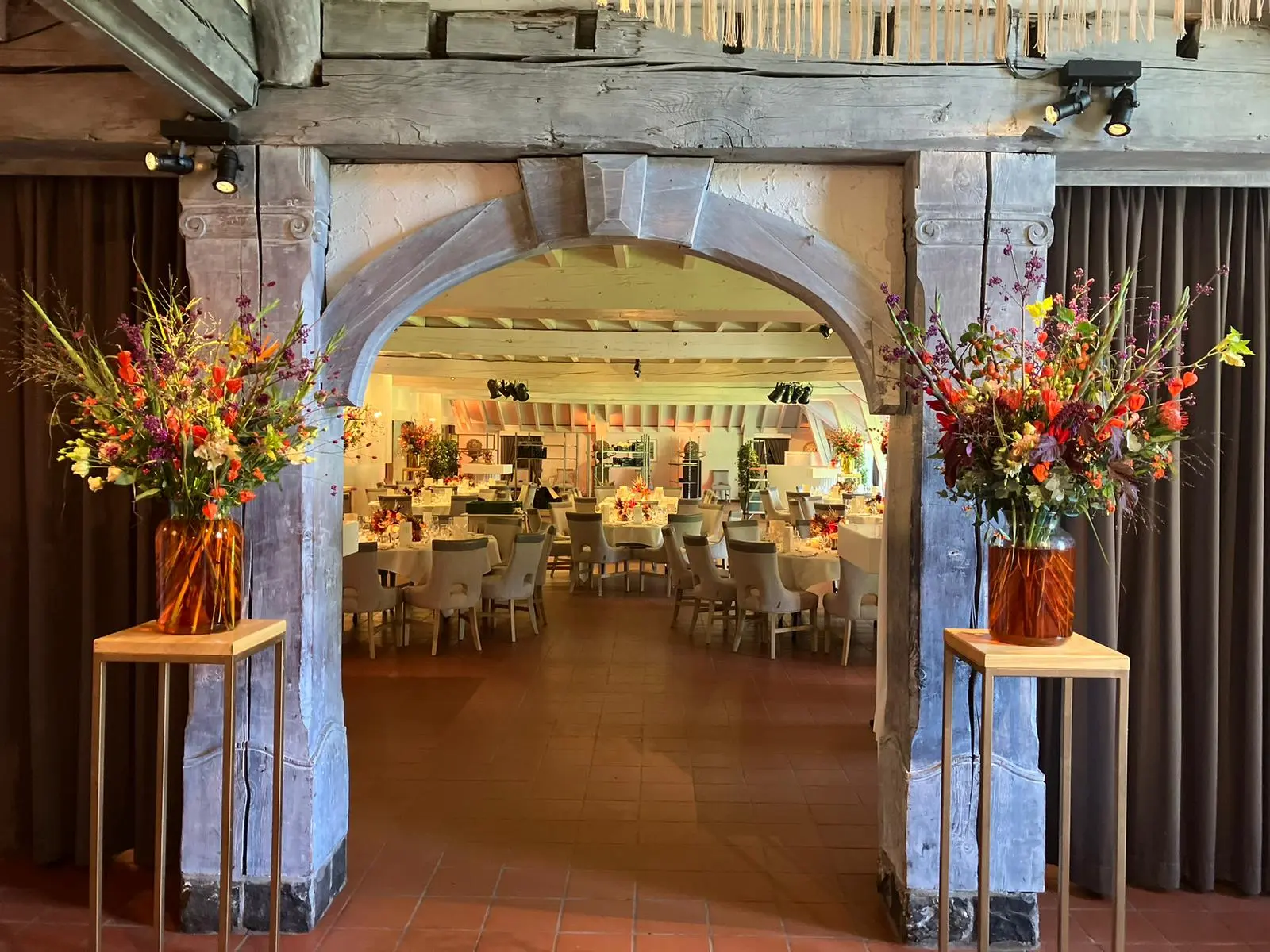 Doorkijk door de poort met bloemstukken naar de gedekte feestzaal