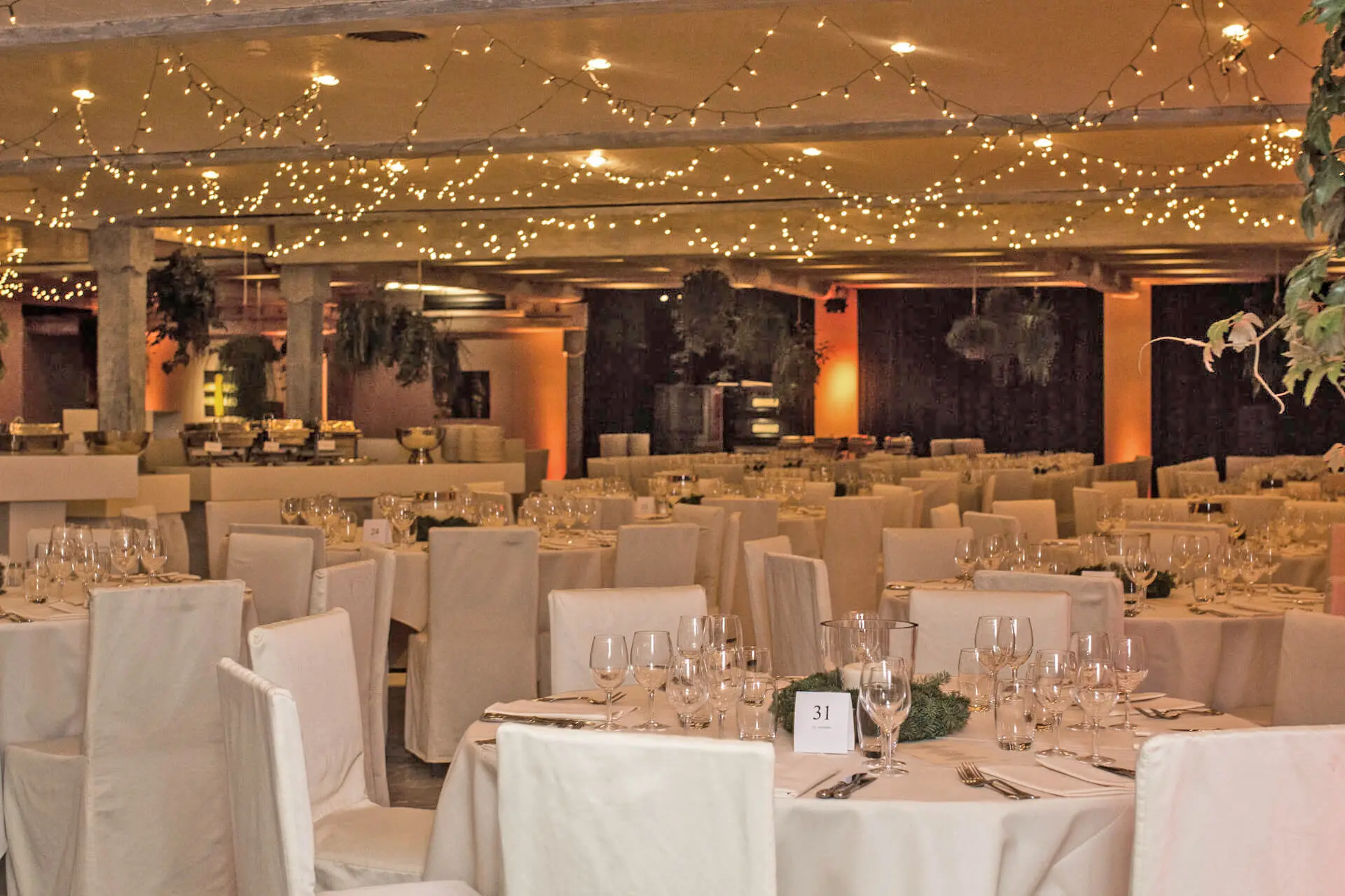 Grote zaal met gedekte tafels onder een plafond vol kerstlichtjes