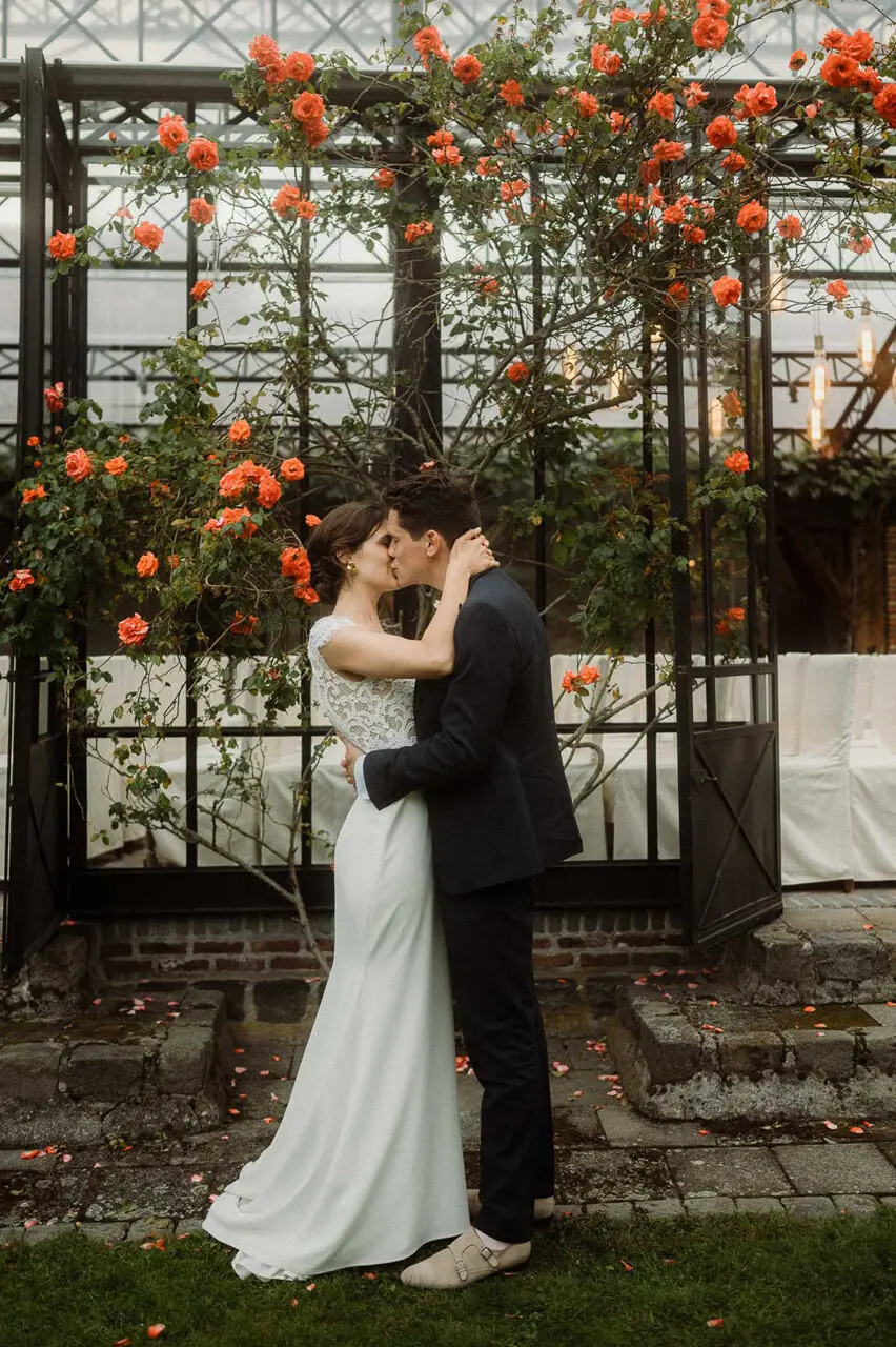 Bruidspaar kust voor de orangerie onder een rozenstruik met oranje bloemen