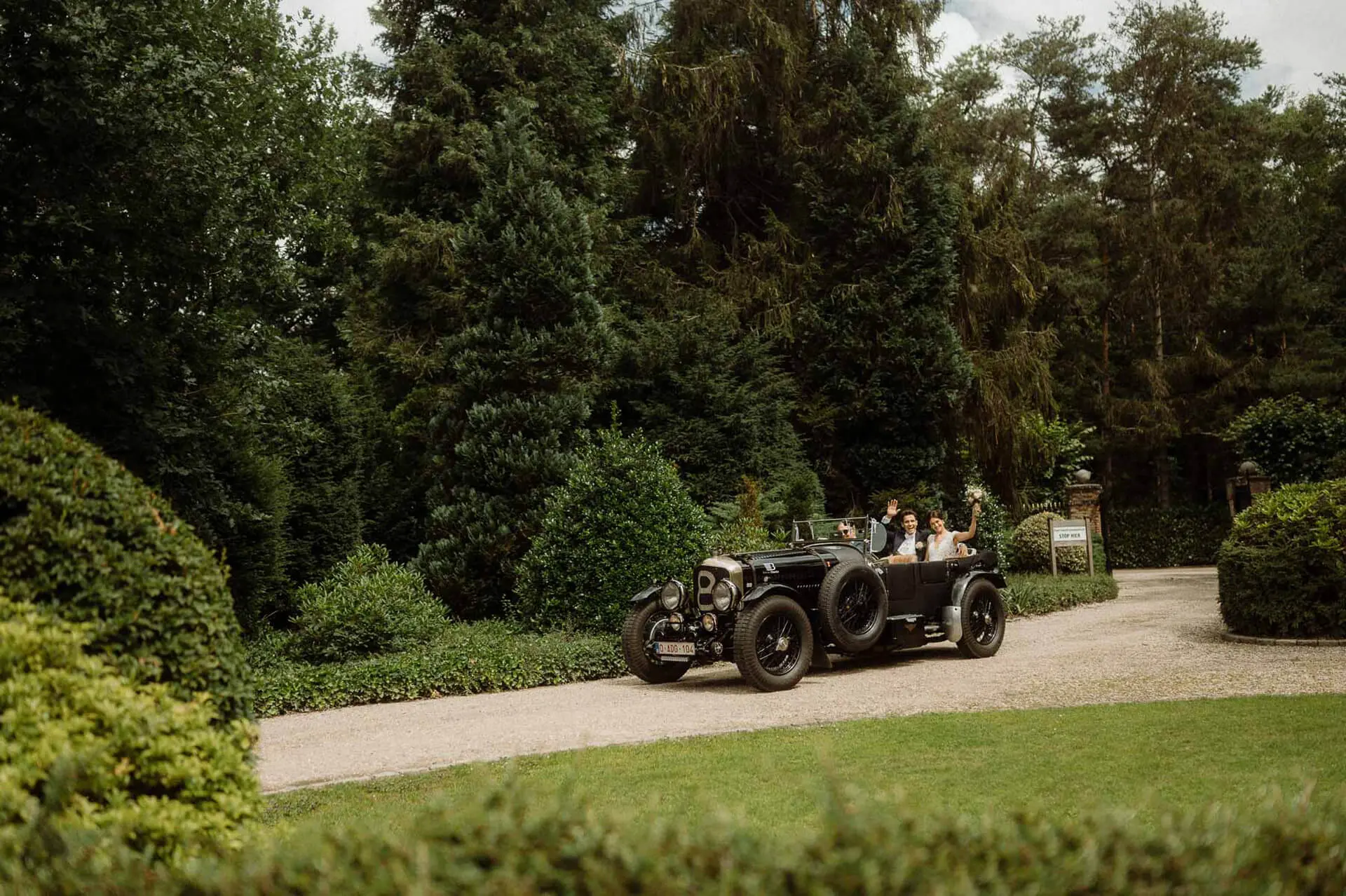 Oldtimer met het bruidspaar rijdt over de oprijlaan tussen het groen