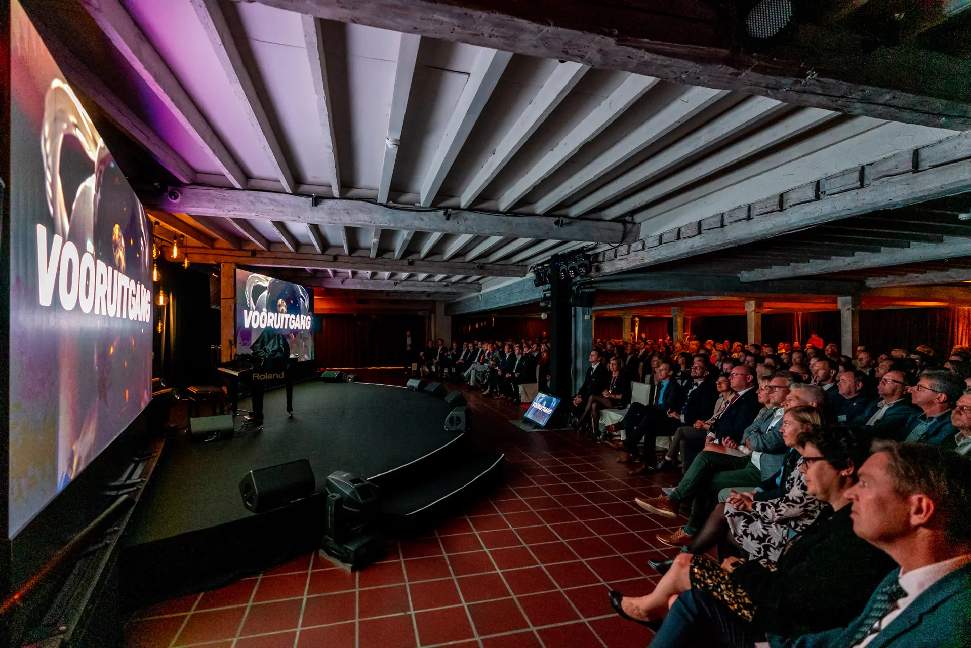 Volle grote zaal van Alta Ripa met podium en groot scherm tijdens een bedrijfsevent