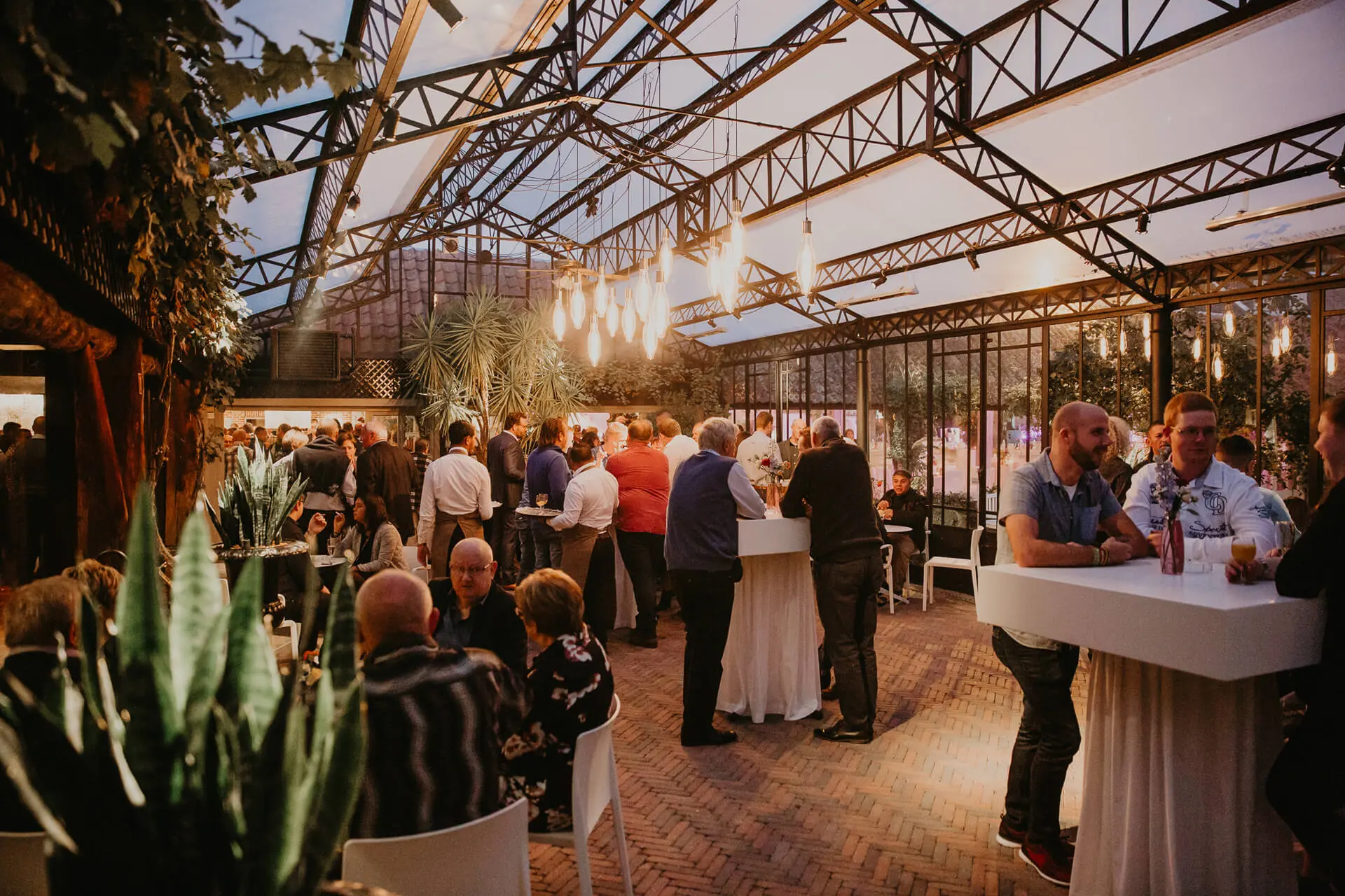 Gasten aan hoge tafels tijdens een receptie in de orangerie van de grote zaal