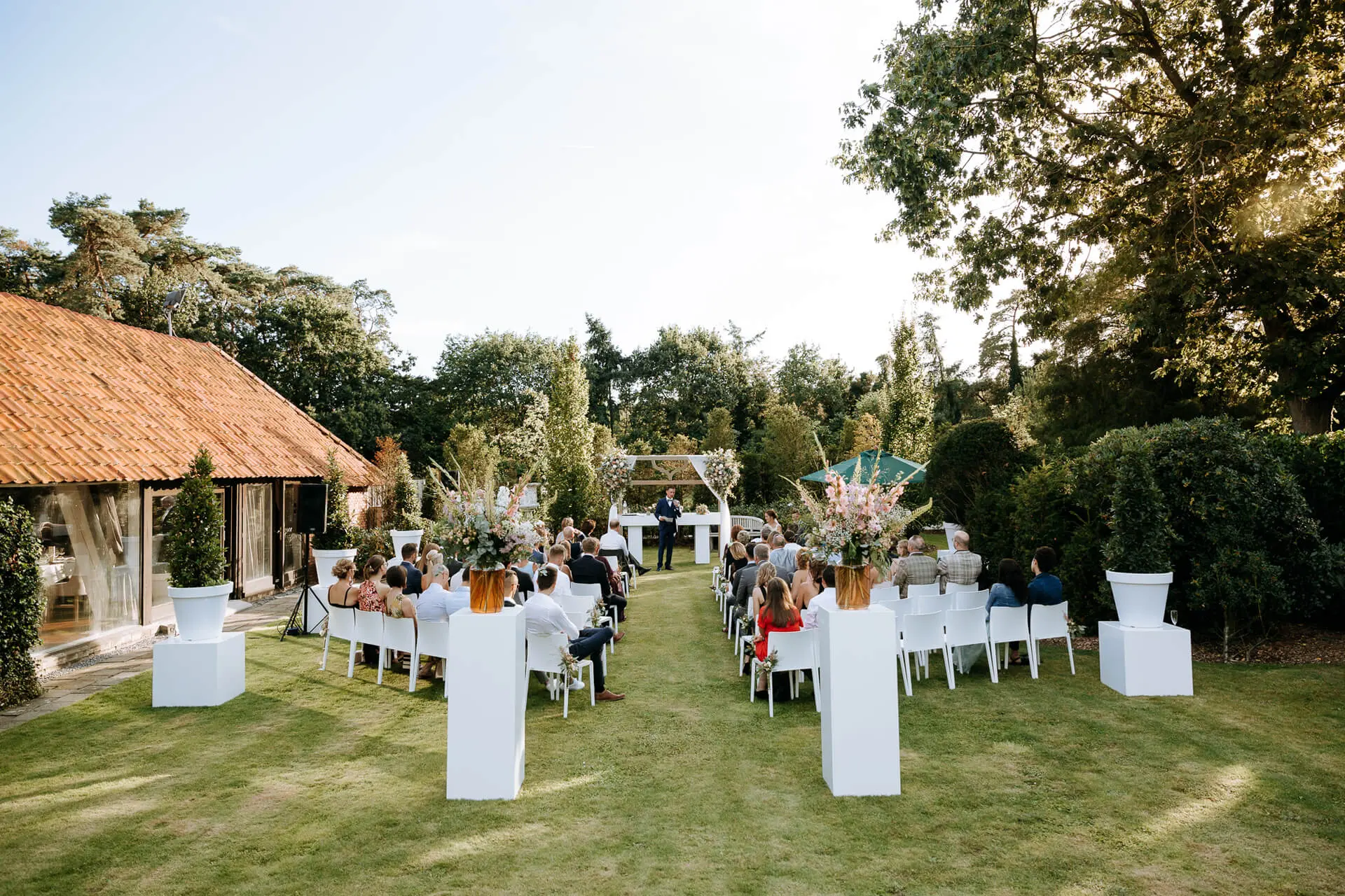 Gasten volgen een huwelijksceremonie in de tuin bij zomers avondlicht