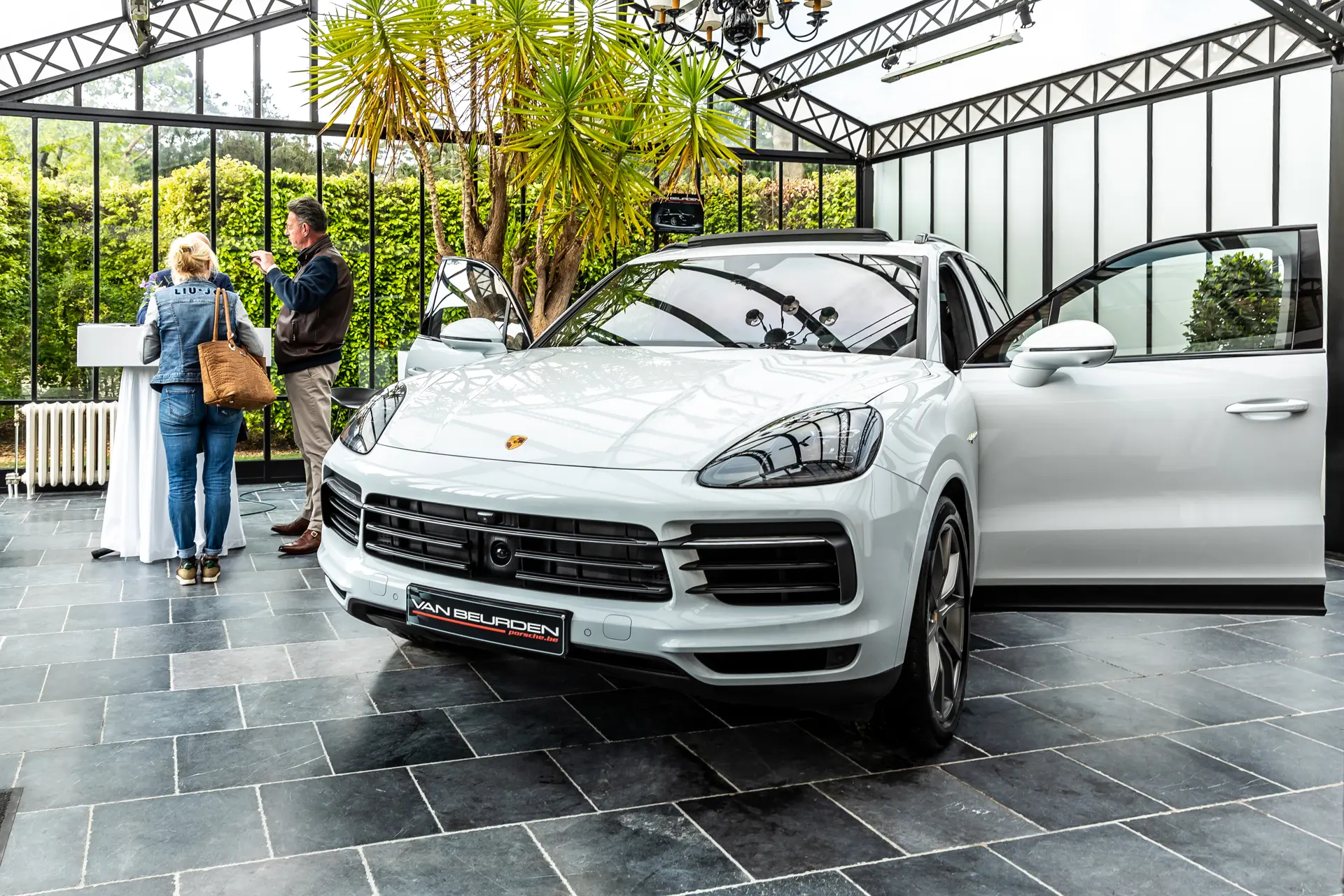 Bezoekers bij een witte Porsche in de orangerie