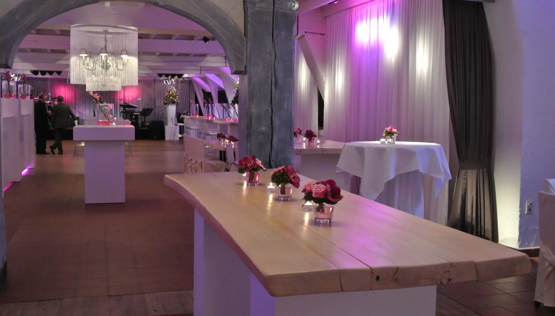 Kleine zaal in lounge-aankleding met een lange houten tafel en paarse verlichting